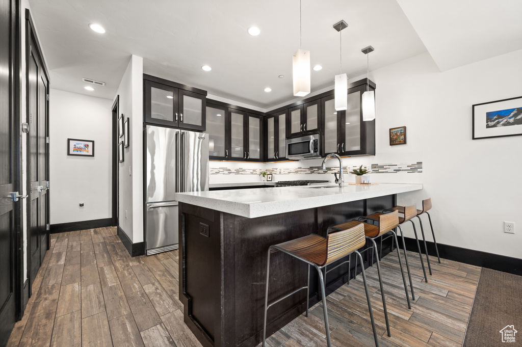 Kitchen with a breakfast bar area, dark wood-type flooring, decorative light fixtures, stainless steel appliances, and light stone countertops