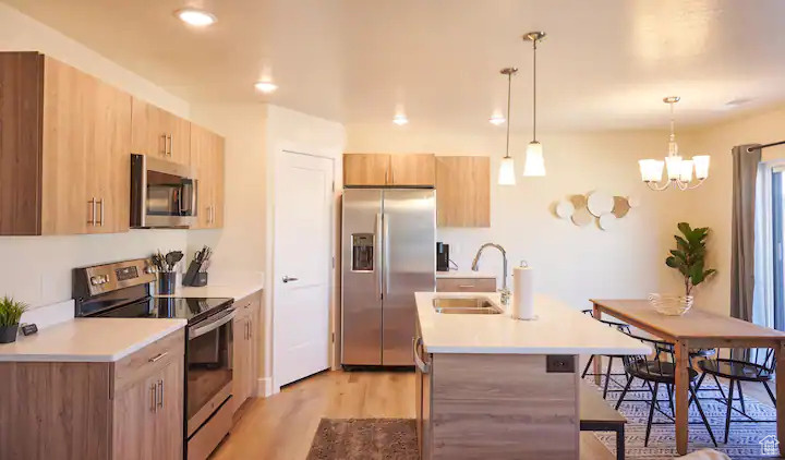Kitchen with decorative light fixtures, appliances with stainless steel finishes, sink, a notable chandelier, and light wood-type flooring