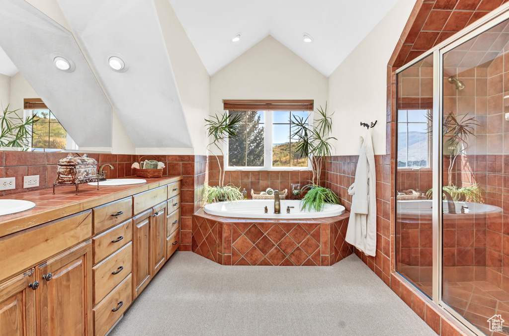 Bathroom with tile walls, double vanity, independent shower and bath, and lofted ceiling