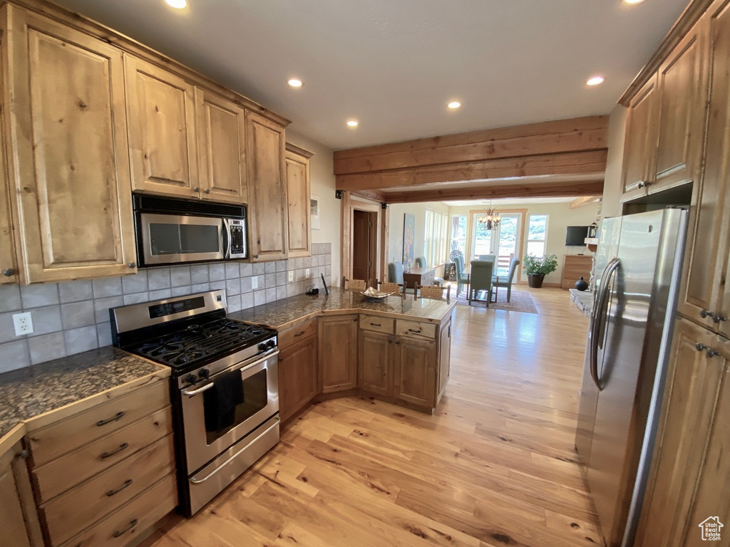 Kitchen featuring light hardwood / wood-style floors, appliances with stainless steel finishes, backsplash, and a notable chandelier
