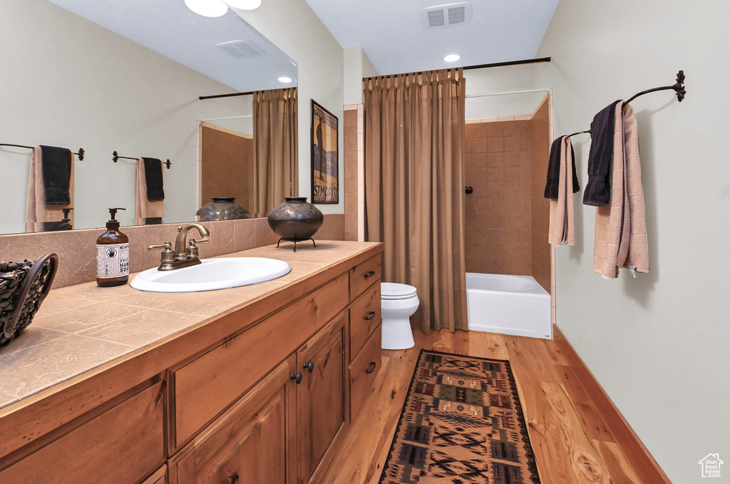 Full bathroom with vanity with extensive cabinet space, toilet, shower / bath combo with shower curtain, and hardwood / wood-style floors