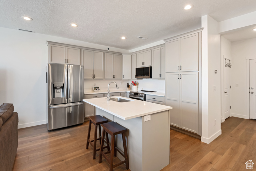 Kitchen featuring appliances with stainless steel finishes, light hardwood / wood-style flooring, a breakfast bar area, a center island with sink, and sink