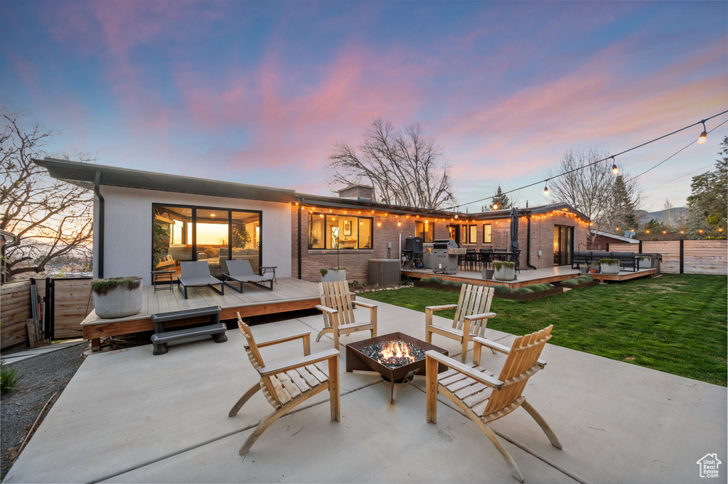 Back house at dusk featuring a patio, a yard, and an outdoor living space with a fire pit