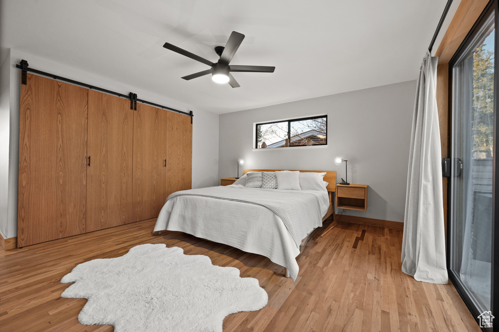 Bedroom featuring light hardwood / wood-style floors, ceiling fan, a barn door, and access to outside