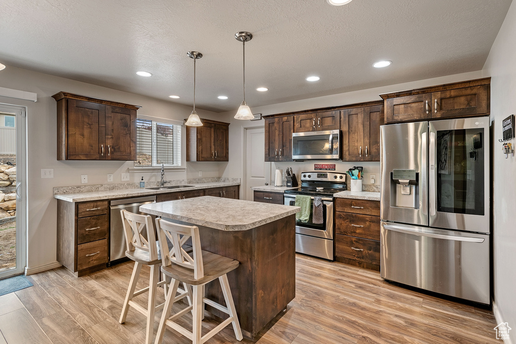 Kitchen featuring a kitchen island, hanging light fixtures, stainless steel appliances, light hardwood / wood-style floors, and sink