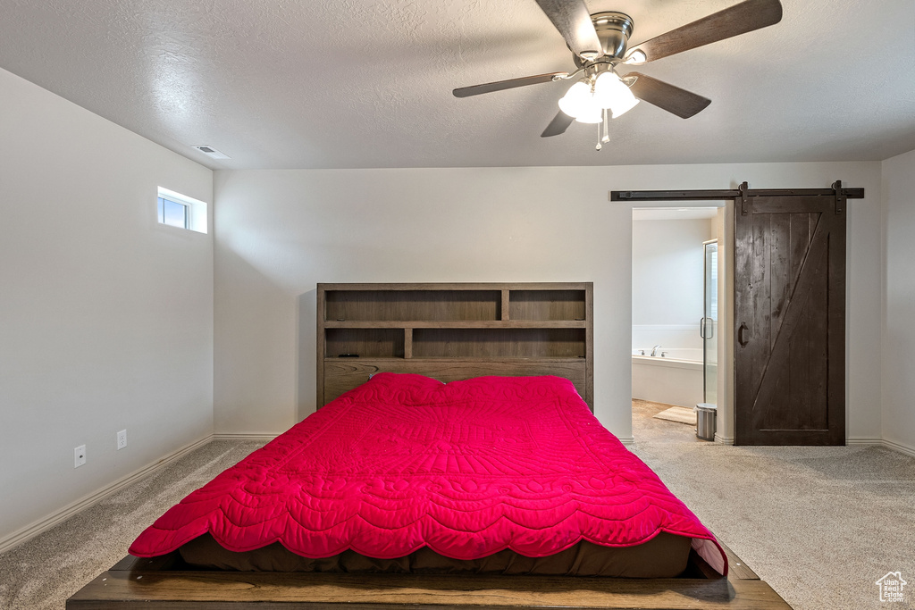 Carpeted bedroom with a textured ceiling, ceiling fan, ensuite bathroom, and a barn door