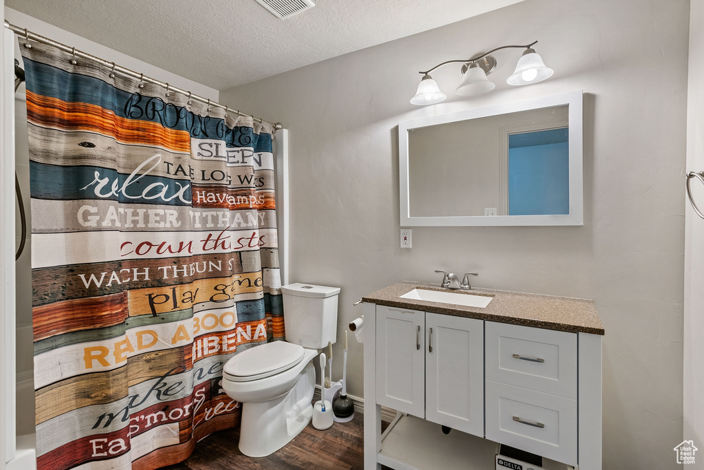 Bathroom featuring a textured ceiling, wood-type flooring, vanity, and toilet