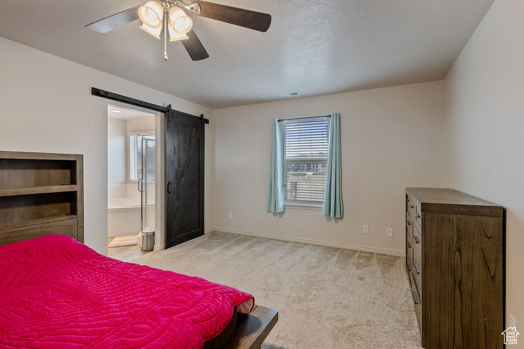 Bedroom featuring light carpet, multiple windows, ceiling fan, and a barn door