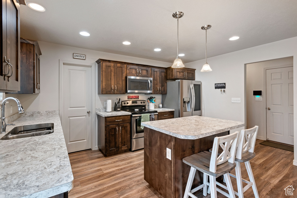 Kitchen with a kitchen breakfast bar, decorative light fixtures, light wood-type flooring, appliances with stainless steel finishes, and sink