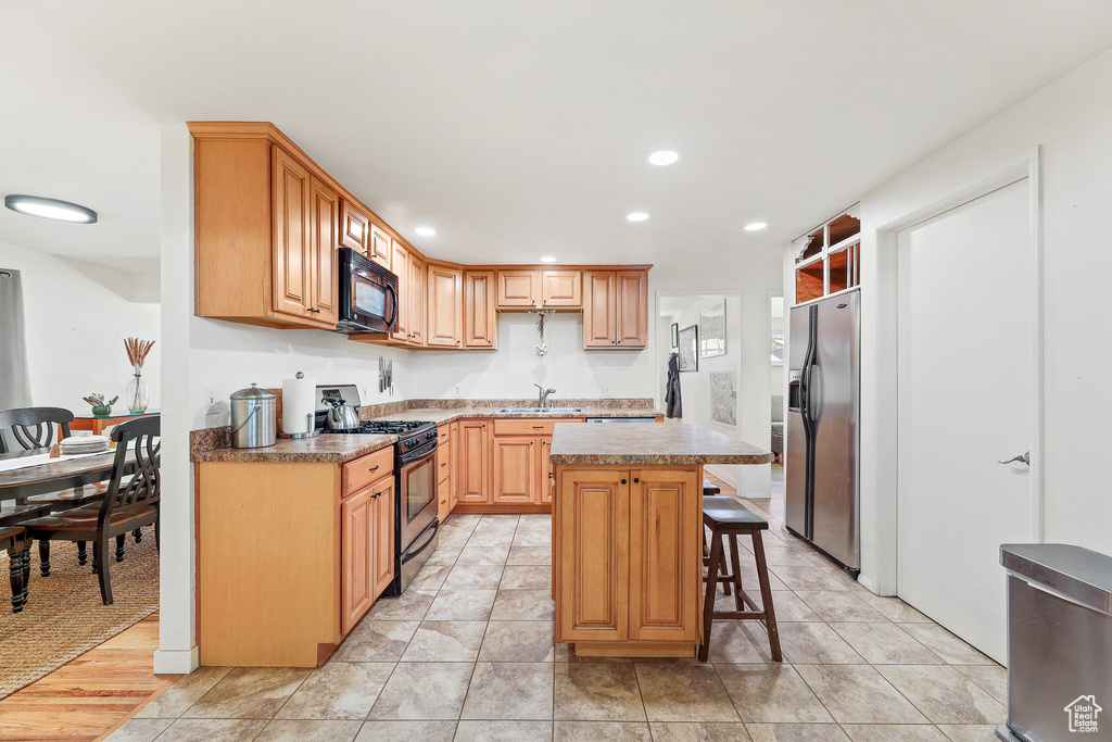Kitchen with a kitchen island, stainless steel appliances, light tile flooring, a kitchen breakfast bar, and sink