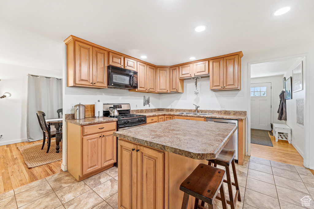 Kitchen with light tile floors, a kitchen island, sink, stainless steel dishwasher, and range with gas stovetop