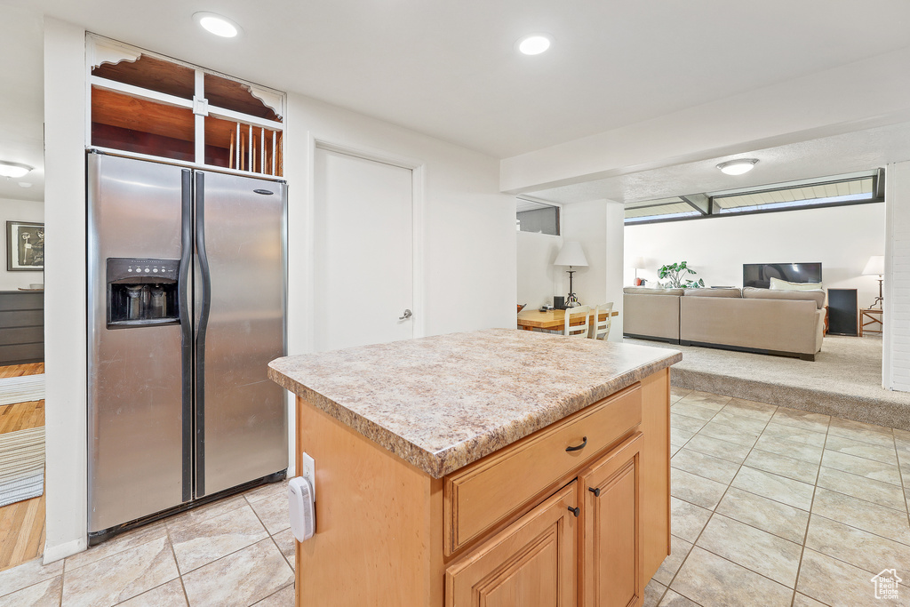 Kitchen with a center island, stainless steel fridge with ice dispenser, and light tile flooring