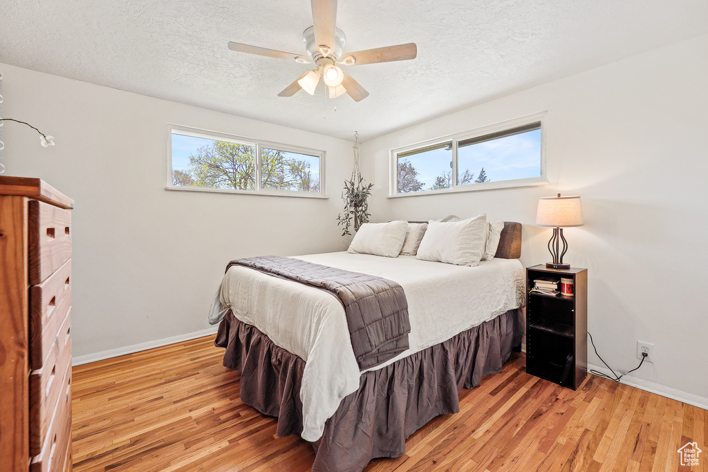 Bedroom featuring light hardwood / wood-style floors, ceiling fan, and a textured ceiling