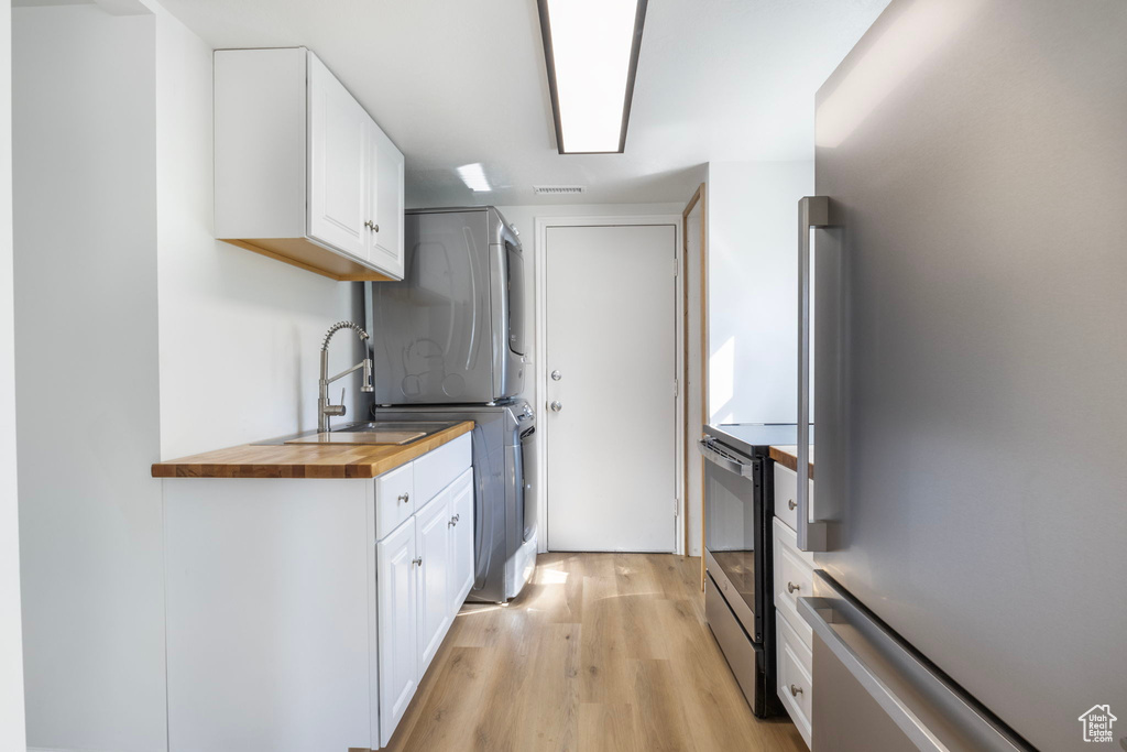 Kitchen with electric stove, light wood-type flooring, white cabinetry, stacked washing maching and dryer, and stainless steel fridge