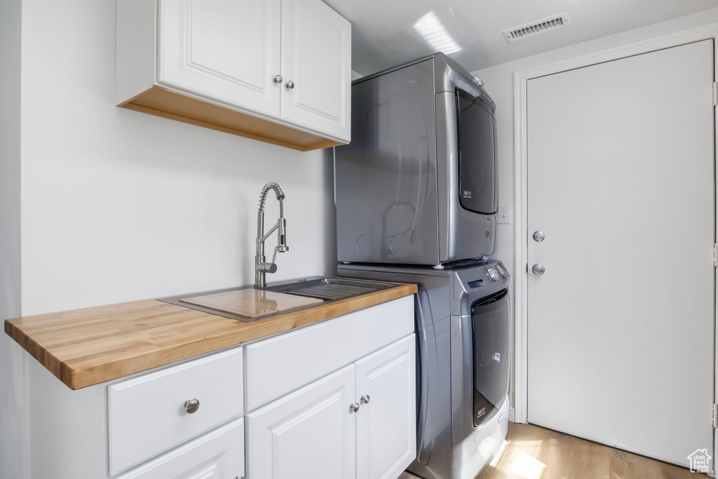 Kitchen with white cabinets, stacked washer and clothes dryer, light wood-type flooring, and sink