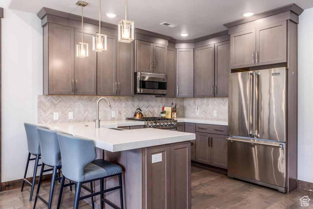 Kitchen featuring hanging light fixtures, a breakfast bar, dark hardwood / wood-style floors, appliances with stainless steel finishes, and sink