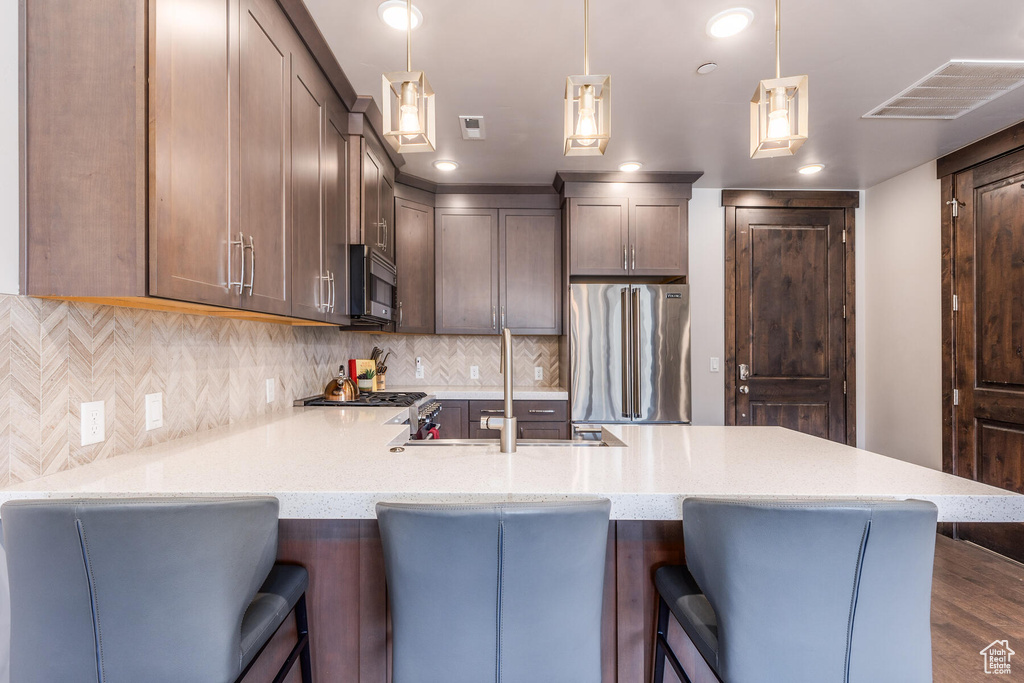 Kitchen featuring light stone countertops, appliances with stainless steel finishes, backsplash, dark hardwood / wood-style flooring, and pendant lighting