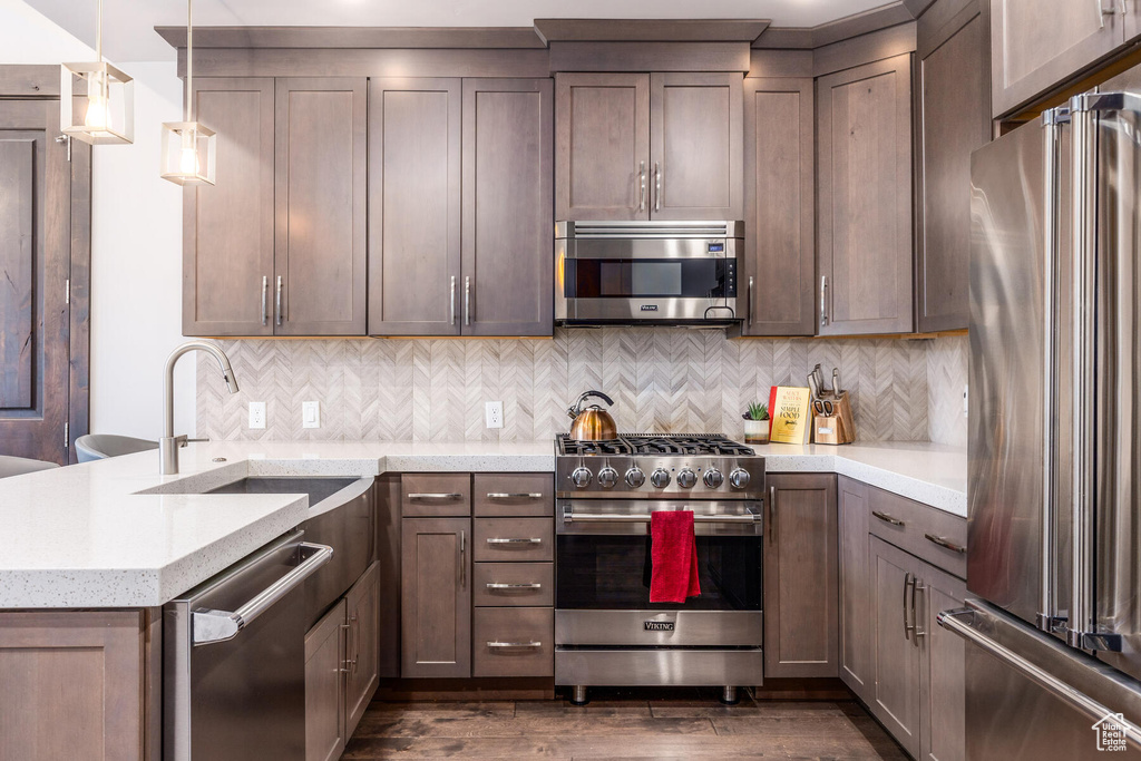Kitchen featuring sink, tasteful backsplash, high end appliances, decorative light fixtures, and dark hardwood / wood-style floors