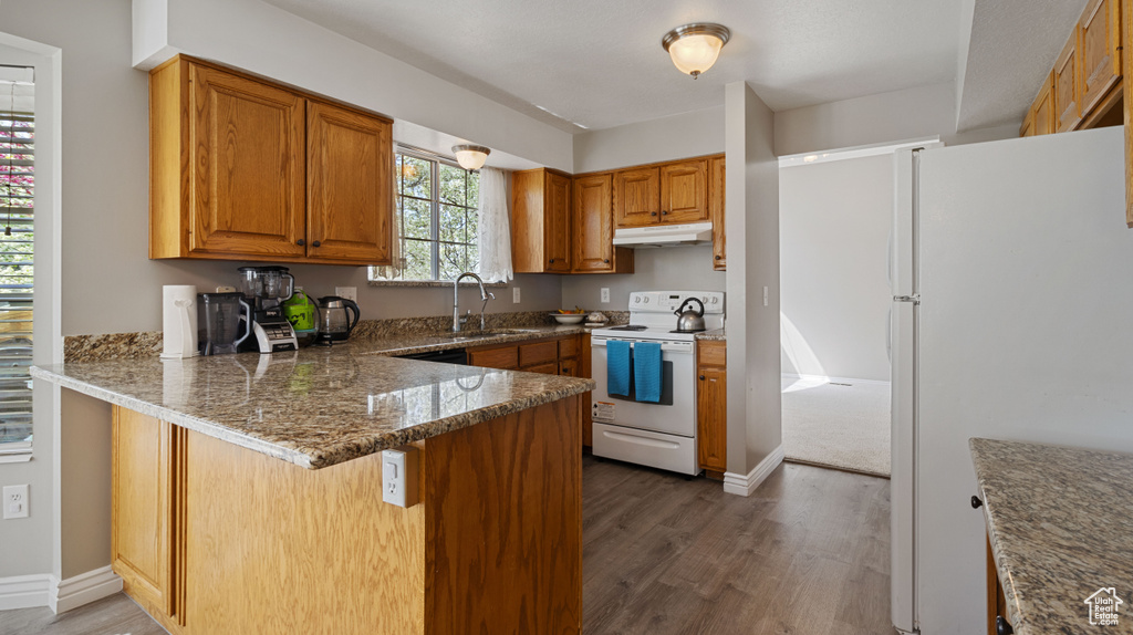Kitchen with white appliances, dark wood-type flooring, kitchen peninsula, sink, and dark stone countertops