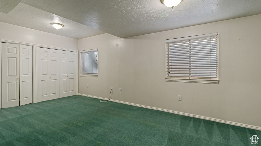 Unfurnished bedroom with dark colored carpet, a textured ceiling, and multiple closets
