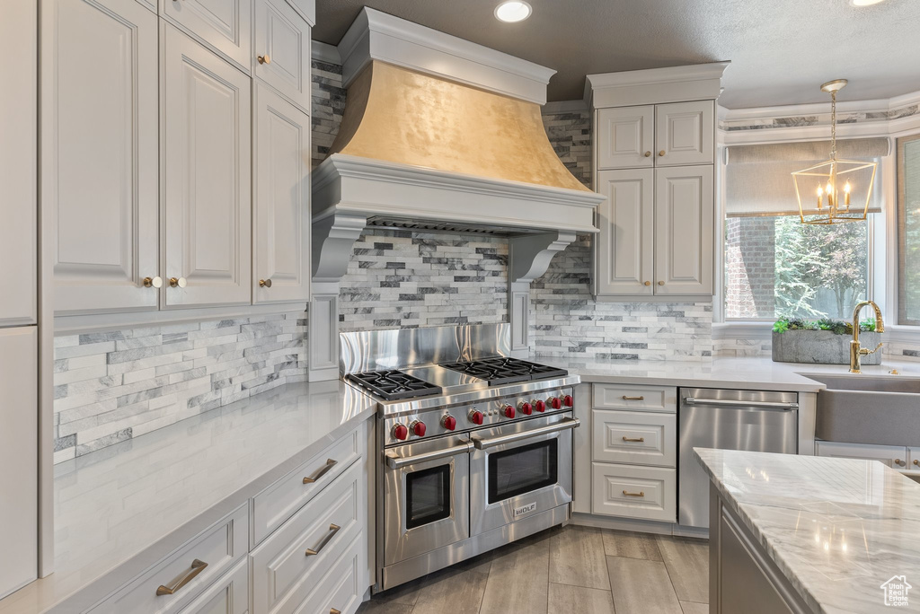 Kitchen featuring light stone counters, appliances with stainless steel finishes, custom exhaust hood, sink, and tasteful backsplash