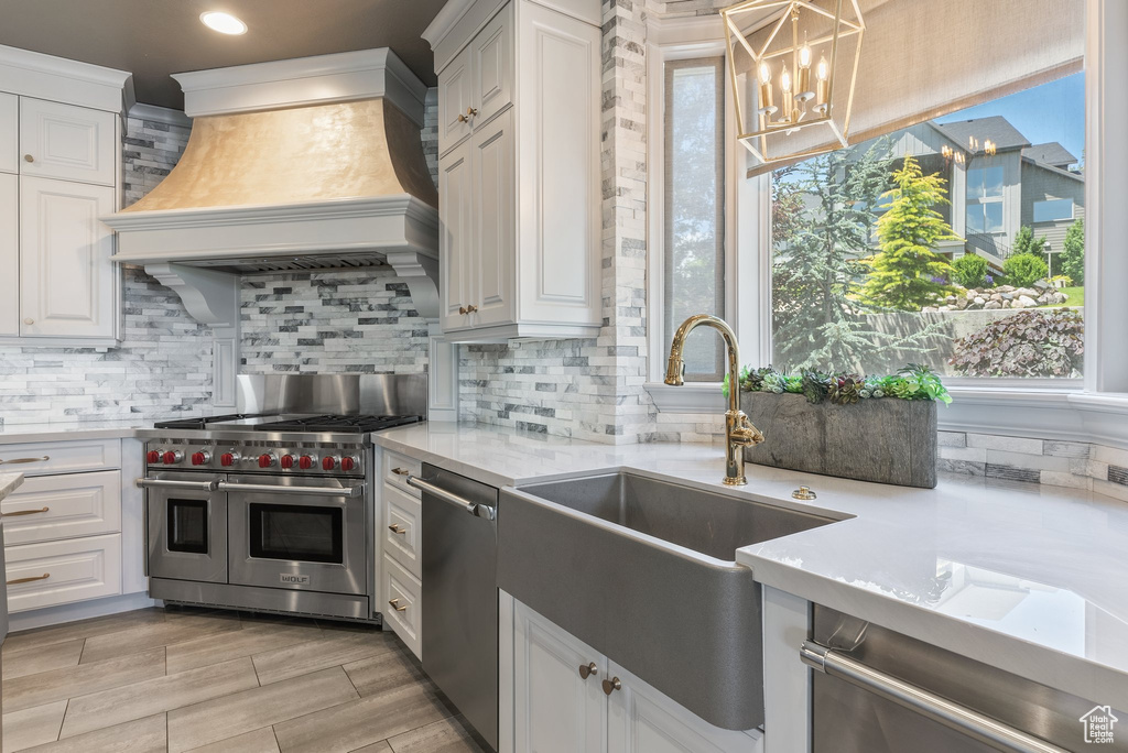 Kitchen featuring custom exhaust hood, white cabinetry, backsplash, appliances with stainless steel finishes, and light stone counters
