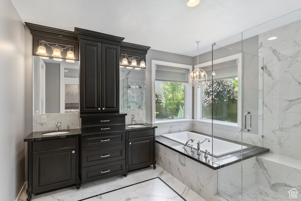 Bathroom featuring dual bowl vanity, backsplash, tile flooring, plus walk in shower, and a chandelier