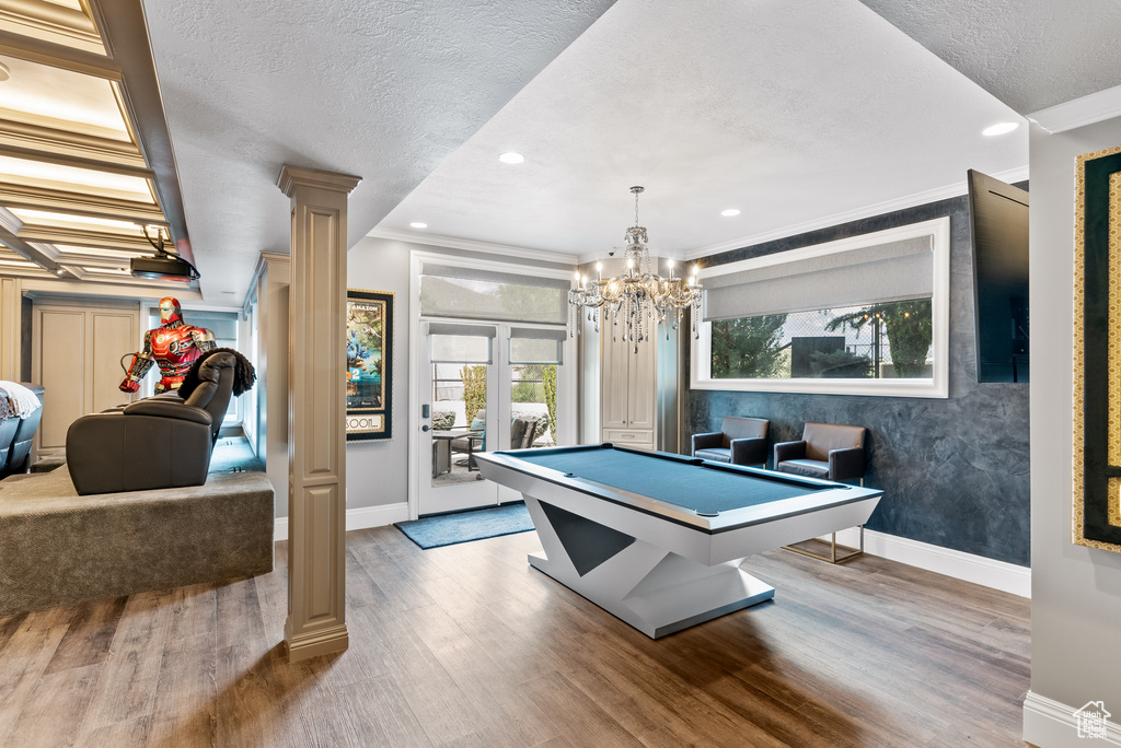 Recreation room with crown molding, an inviting chandelier, pool table, hardwood / wood-style flooring, and ornate columns