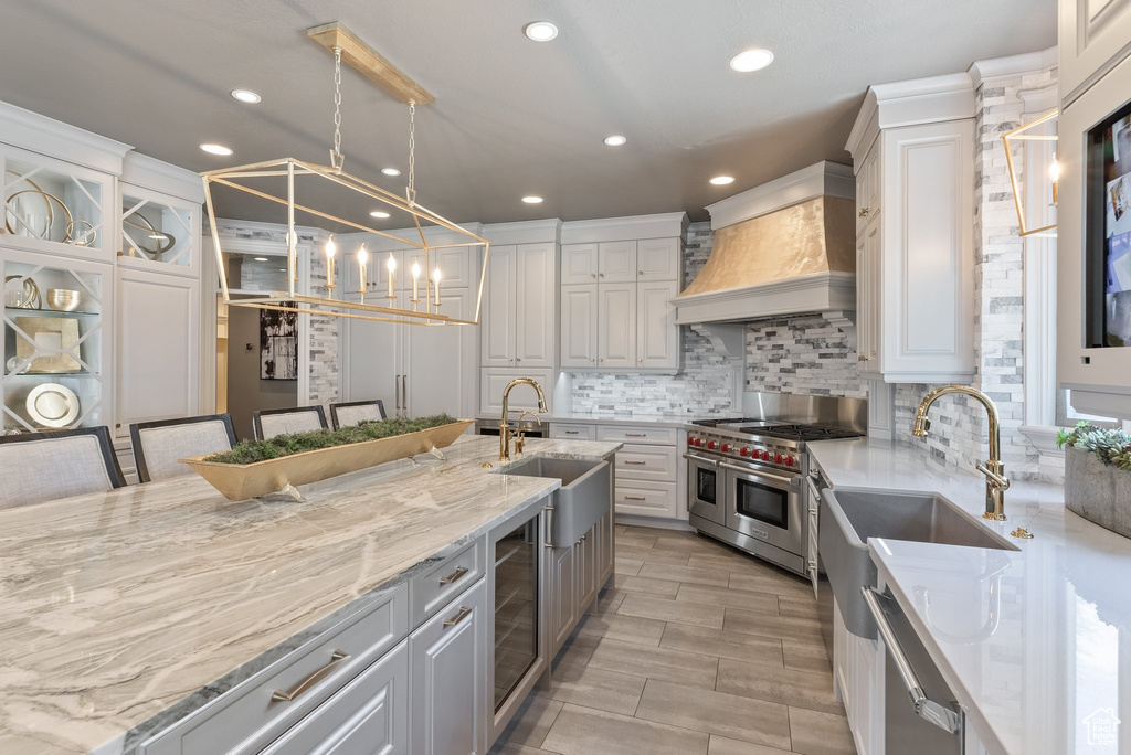Kitchen with light stone countertops, appliances with stainless steel finishes, tasteful backsplash, custom exhaust hood, and white cabinets
