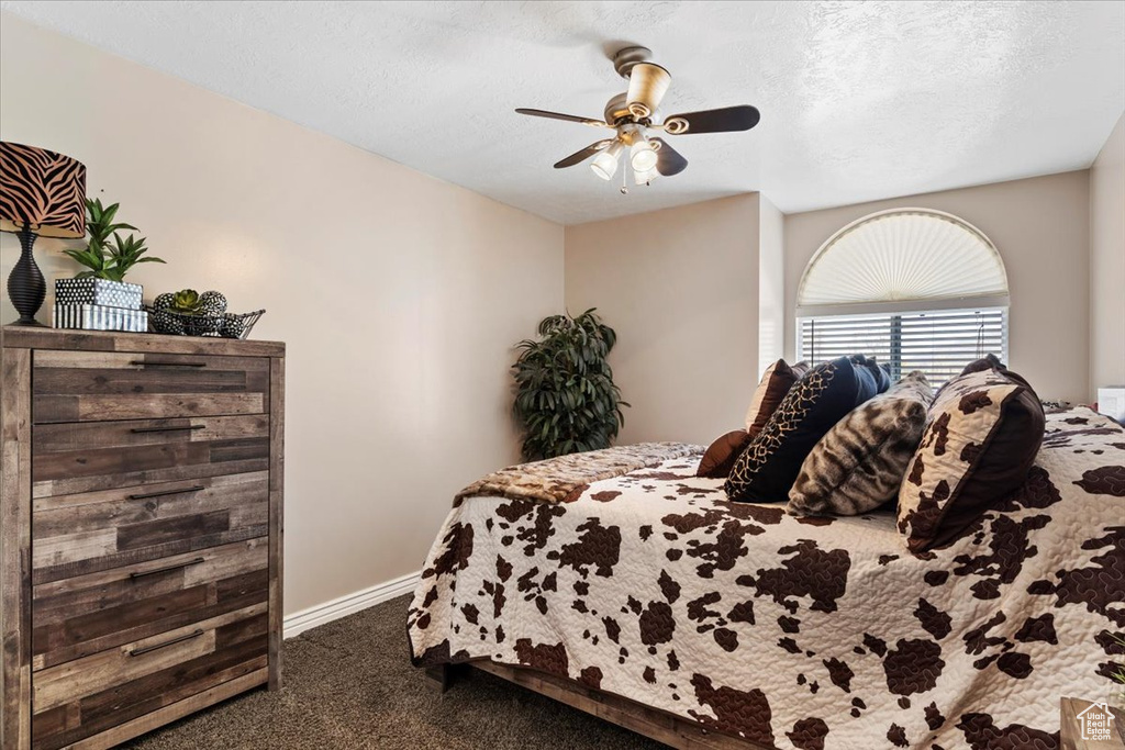 Bedroom featuring a textured ceiling, ceiling fan, and dark colored carpet