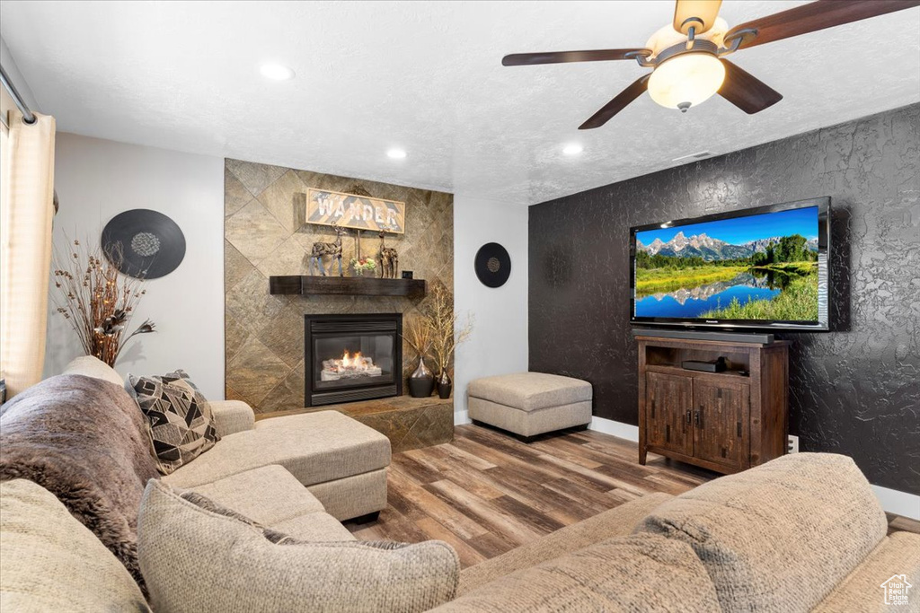 Living room featuring a textured ceiling, ceiling fan, a fireplace, and dark wood-type flooring