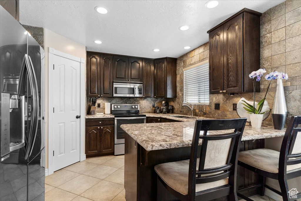 Kitchen with sink, a kitchen breakfast bar, appliances with stainless steel finishes, and light tile floors