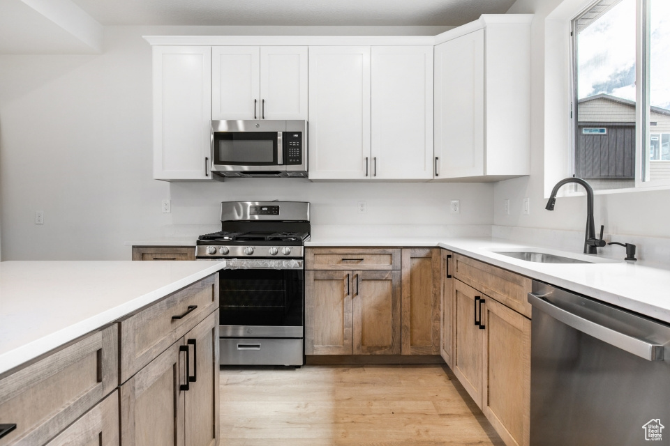 Kitchen with appliances with stainless steel finishes, light hardwood / wood-style flooring, sink, and white cabinetry