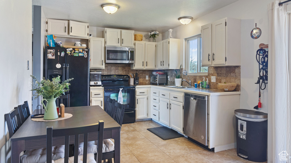 Kitchen with light tile floors, white cabinets, sink, backsplash, and black appliances