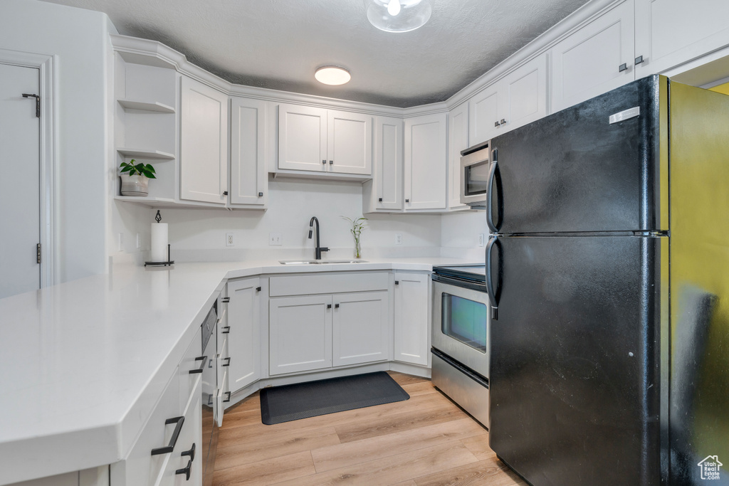 Kitchen with black fridge, light hardwood / wood-style flooring, range, white cabinets, and sink
