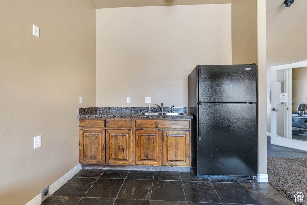 Kitchen featuring dark stone countertops, sink, black refrigerator, and dark tile floors