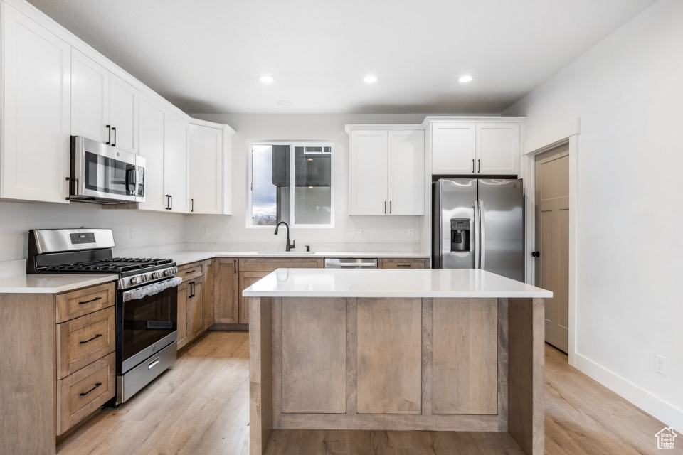 Kitchen featuring white cabinets, light hardwood / wood-style floors, appliances with stainless steel finishes, and a center island