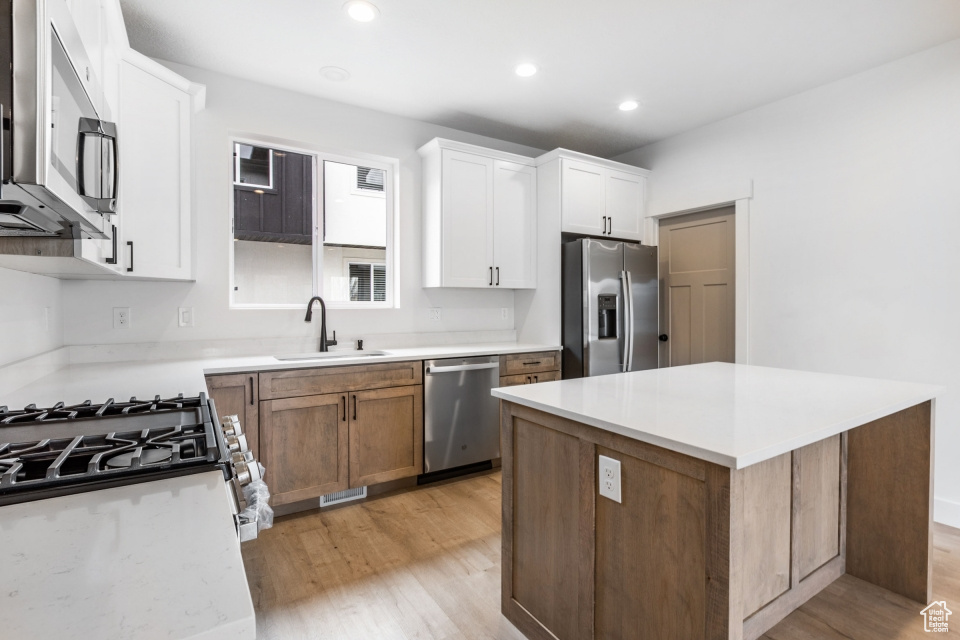 Kitchen featuring white cabinets, appliances with stainless steel finishes, sink, light stone counters, and light hardwood / wood-style floors