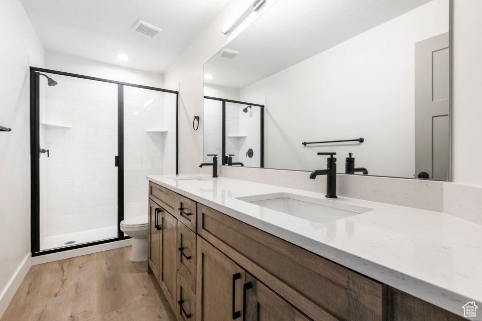 Bathroom with a shower with shower door, vanity with extensive cabinet space, toilet, hardwood / wood-style flooring, and dual sinks