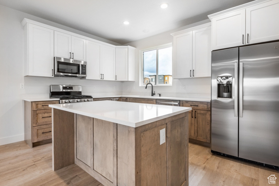 Kitchen featuring appliances with stainless steel finishes, a center island, white cabinets, sink, and light hardwood / wood-style floors