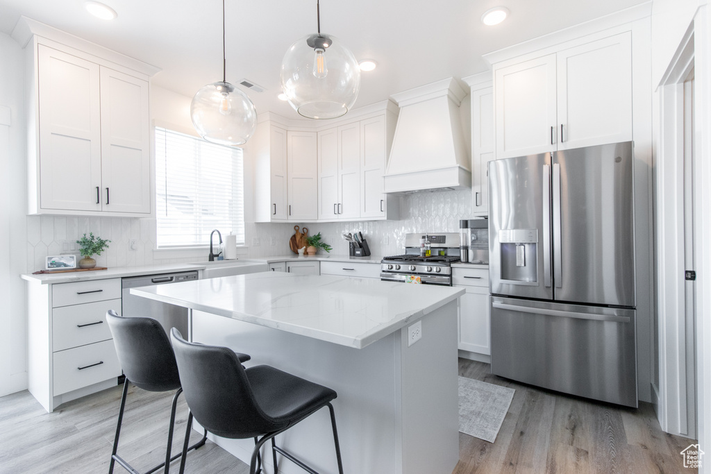 Kitchen with light hardwood / wood-style floors, appliances with stainless steel finishes, backsplash, and custom range hood