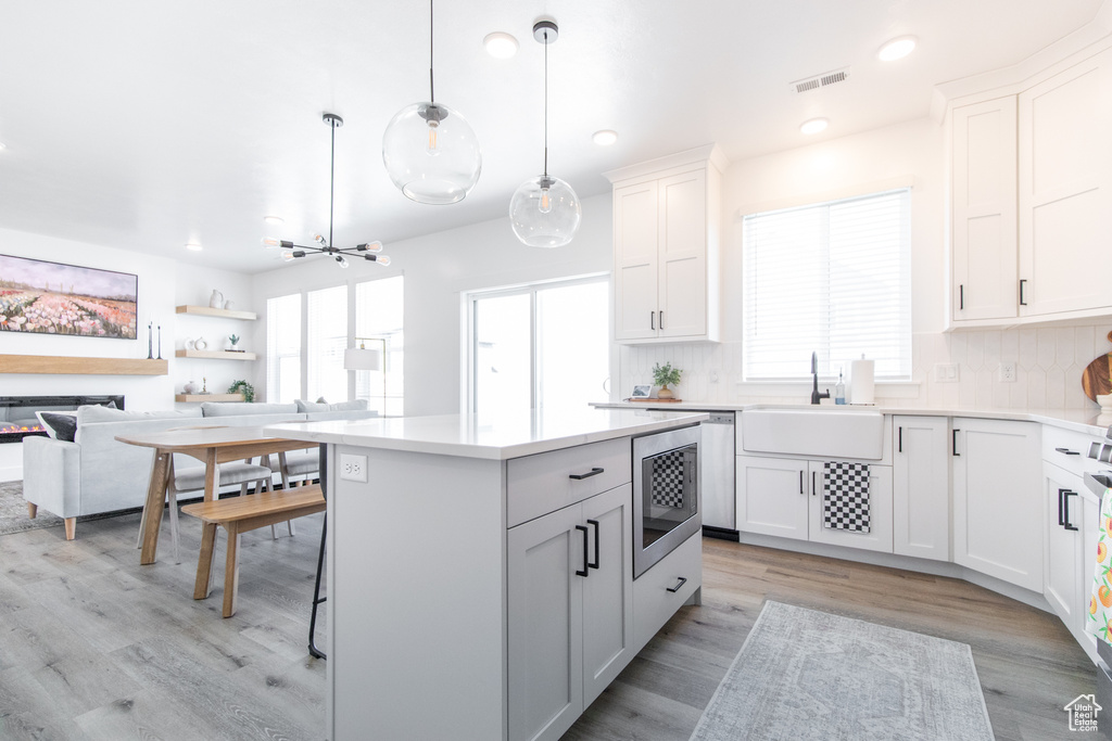 Kitchen with white cabinets, sink, backsplash, hanging light fixtures, and light hardwood / wood-style flooring