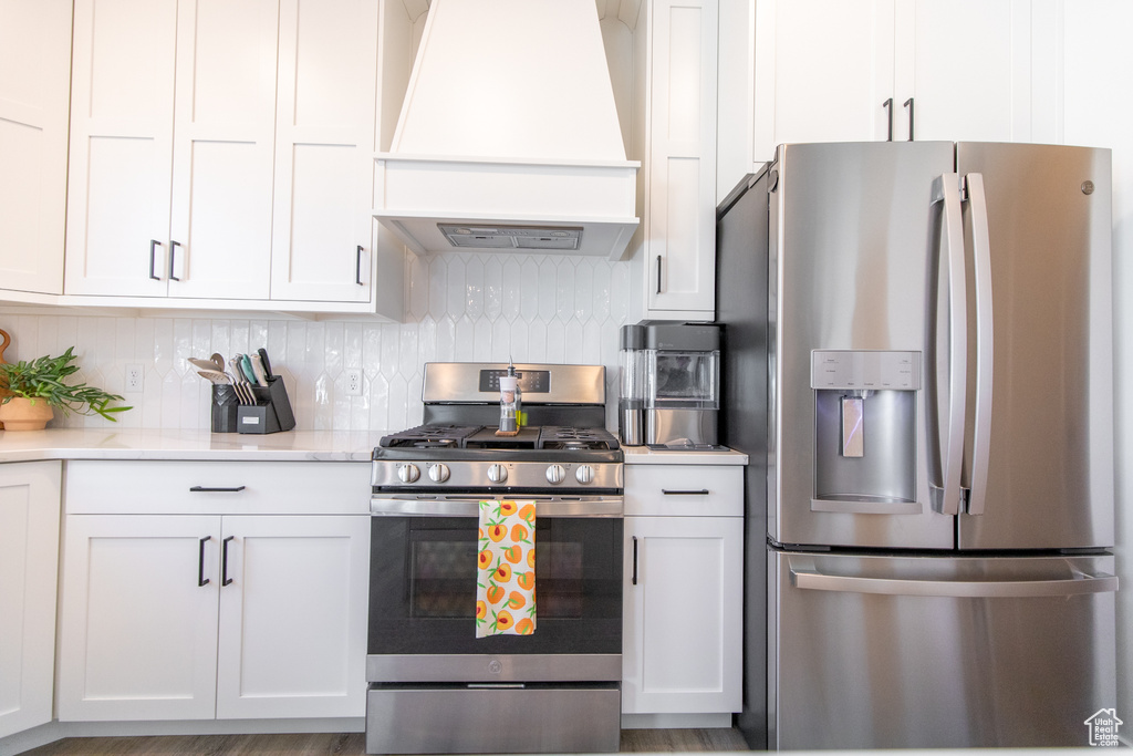 Kitchen featuring backsplash, appliances with stainless steel finishes, white cabinetry, and custom range hood