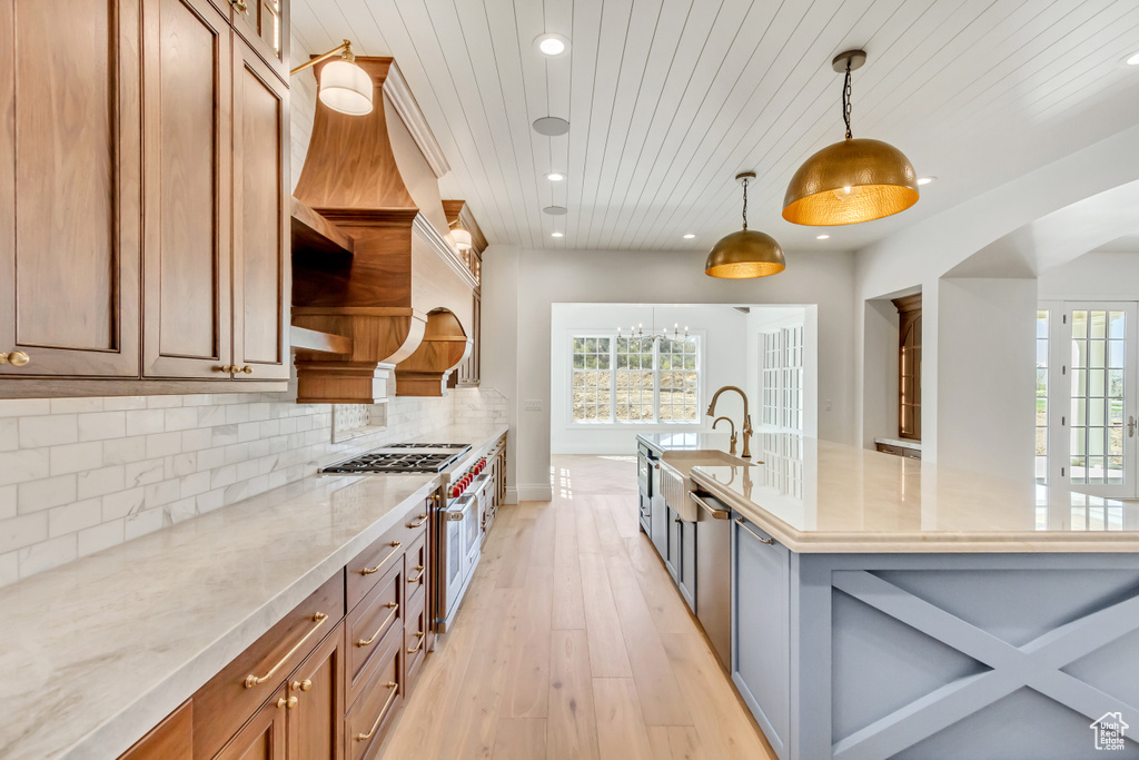 Kitchen featuring light stone countertops, backsplash, double oven range, pendant lighting, and light wood-type flooring