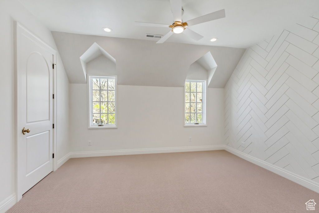 Additional living space with a healthy amount of sunlight, ceiling fan, vaulted ceiling, and light carpet