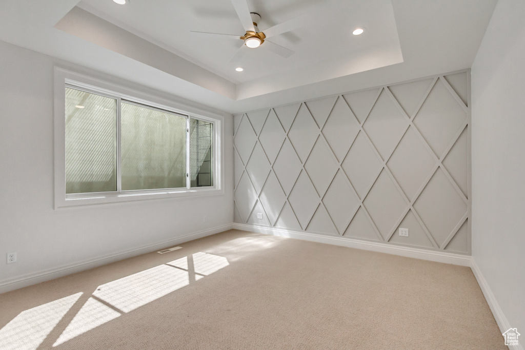 Empty room with light carpet, ceiling fan, and a tray ceiling