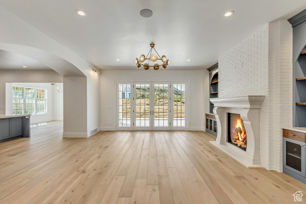 Unfurnished living room featuring a healthy amount of sunlight, light hardwood / wood-style flooring, and a brick fireplace