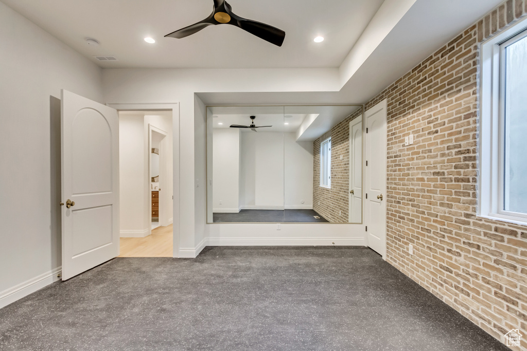 Interior space with light colored carpet, ceiling fan, and brick wall