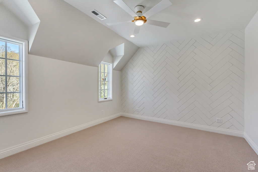 Additional living space featuring light colored carpet, vaulted ceiling, and a healthy amount of sunlight