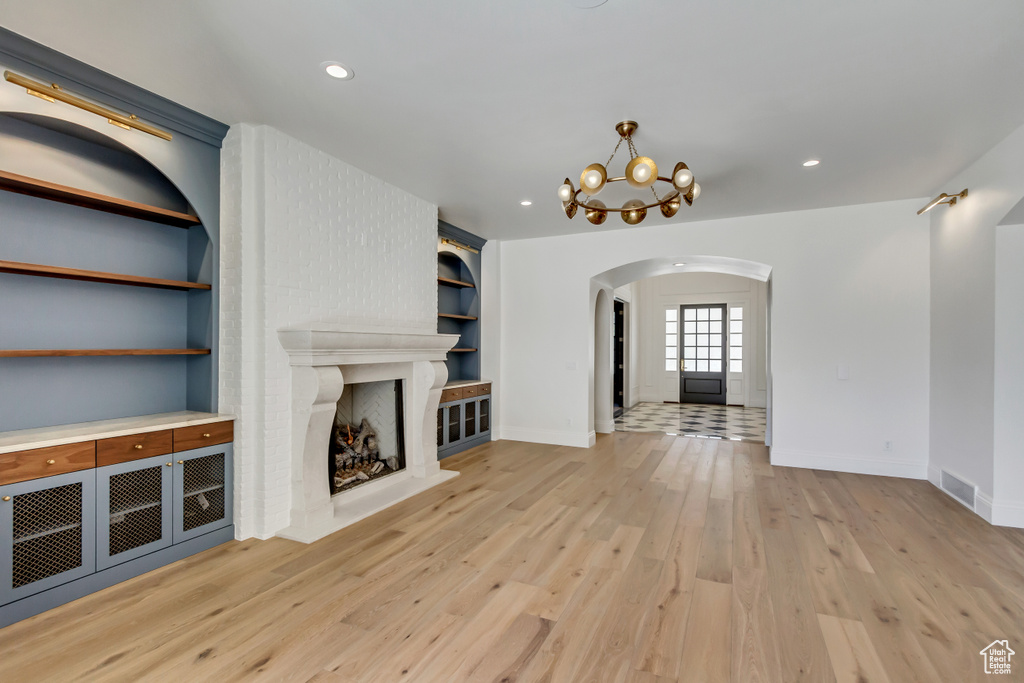 Unfurnished living room with built in features, light hardwood / wood-style floors, a brick fireplace, and a notable chandelier